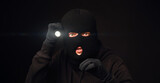 Masked burglar with flashlight on dark back