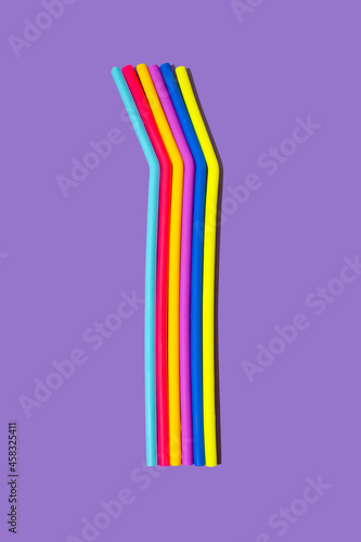 Vivid neon straws in rainbow colours against purple background. Minimal creative cyberpunk concept.