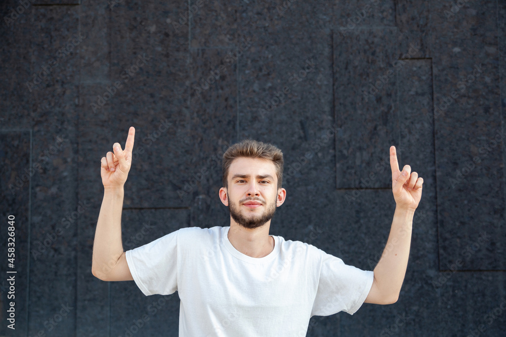 Gesture, emotion, expression and people concept - European bearded man in a white T-shirt pointing fingers up at the copy space on the street against a dark background Gesture, emotion, expression and people concept - European bearded man in a white T-shirt pointing fingers up at the copy space on the street against a dark background