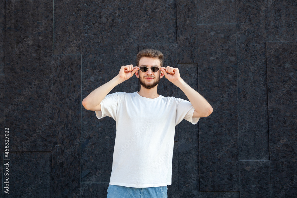 Gesture, emotion, expression and people concept - Caucasian bearded man in white T-shirt and jeans wearing sunglasses over his eyes with copy space outside on a black background