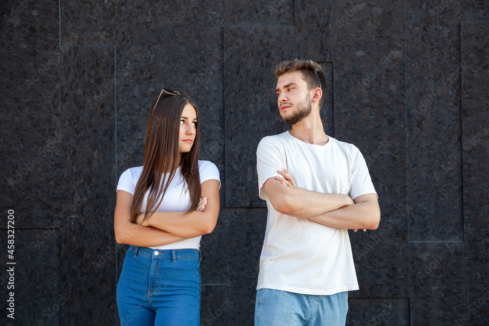 Emotions, gesture, expression and people concept - Offended Caucasian man and woman looking at each other and standing in white T-shirts with arms crossed on a black background with copy space