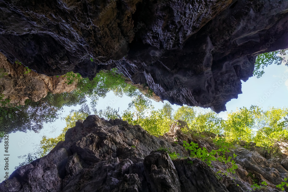 Gorge seen from below. Deep gorge surrounded by millenary rocks, viewed from below. On the edges the luxuriant vegetation and the background sky.