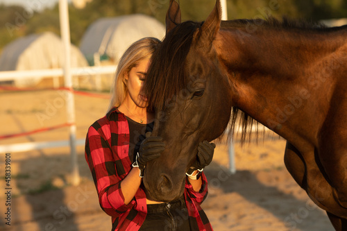 Obraz na plátně Young woman farmer in a red checkered shirt hugs her horse concept of love between people and animals