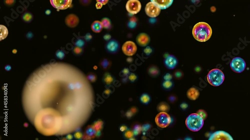 Many rainbow bright soap bubbles fly and burst on a black background. Multicolored round bubbles move in space in slow motion and shimmers in the rays of light. Close up.