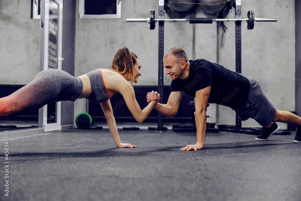 Obraz premium Motivation and support in training, sports lifestyle. The couple does sports exercises together. They are in push ups position and holding hands to maintain body balance. Fitness challenge