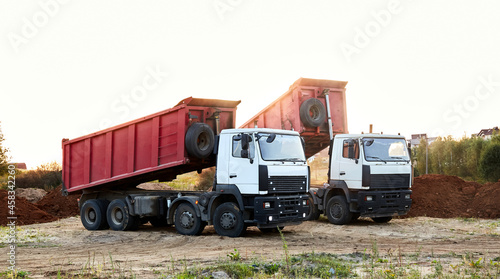 Fotografie Two red dump trucks simultaneously lifted the bodies to unload the sand
