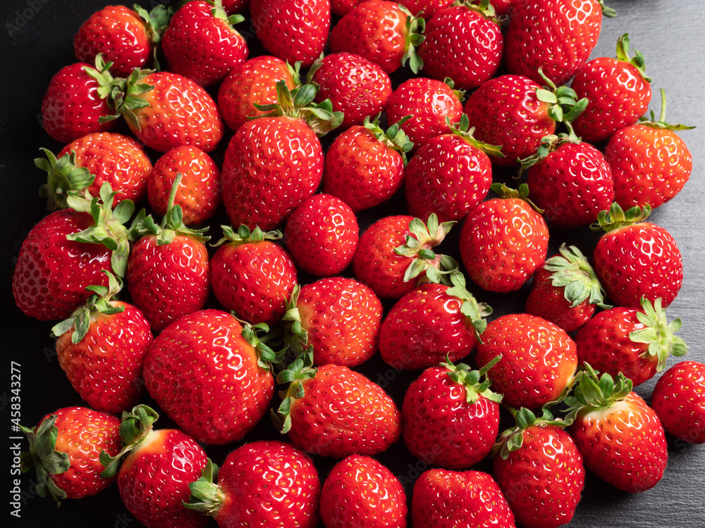 A lot of red ripe and fresh strawberries on black slate background A lot of red ripe and fresh strawberries on black slate background