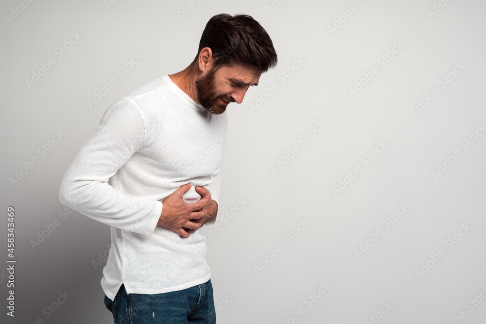 Young man having a stomachache. Young man keeping hands at his stomach because painful disease feeling unwell. Ache concept Young man having a stomachache. Young man keeping hands at his stomach because painful disease feeling unwell. Ache concept