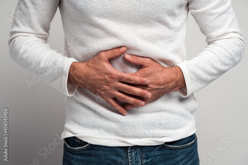 Close up view of the man holding hands on stomach feeling acute pain, suffering indigestion and nausea, duodenal ulcer. Indoor studio shot isolated on white background photo