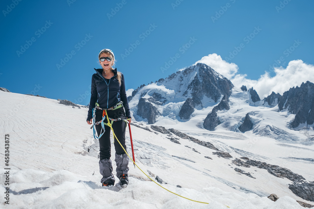 Happy cheerful sincerely laughing young female portrait in climbing harness, crampons, sunglasses, mountain team rope while she descending after successful mountain climbing. Happy active people image Happy cheerful sincerely laughing young female portrait in climbing harness, crampons, sunglasses, mountain team rope while she descending after successful mountain climbing. Happy active people image