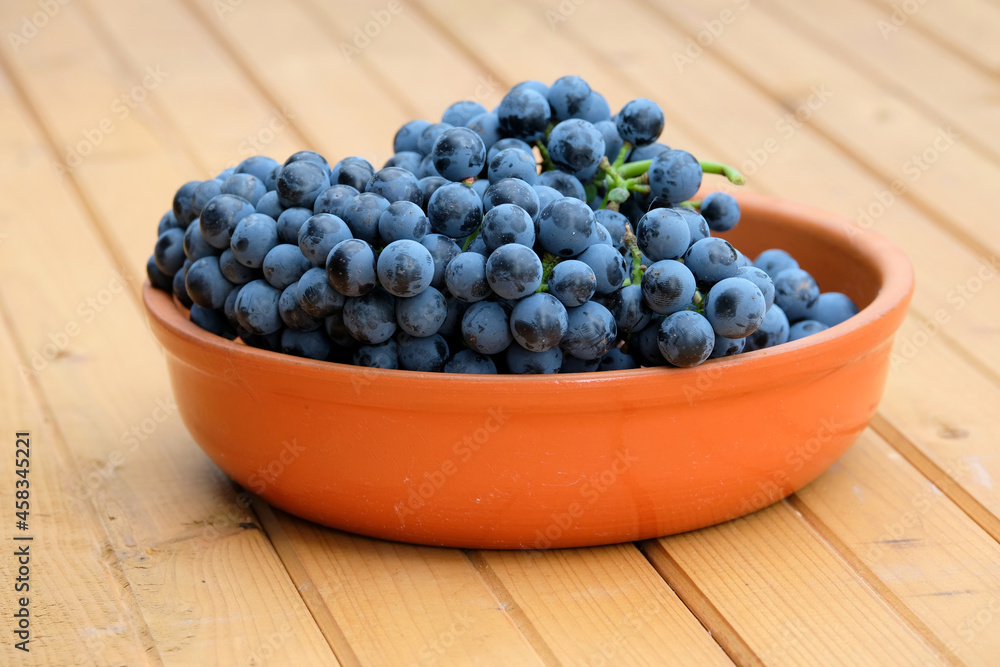 Lot of ripe red grape berries on bunch in brown round bowl on wooden table front view close-up Lot of ripe red grape berries on bunch in brown round bowl on wooden table front view close-up