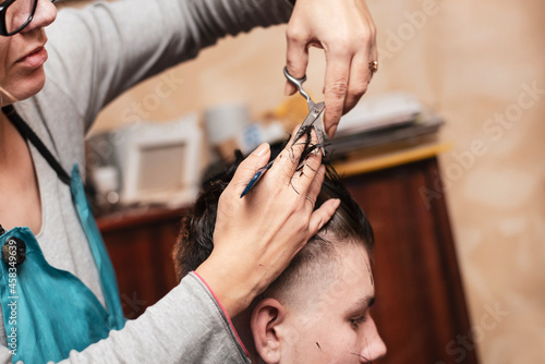 In the evening, a woman cuts her teenage son's hair at home and makes him a modern hairstyle