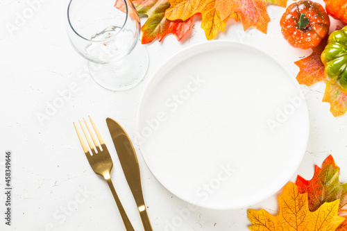 Fototapeta Naklejka Na Ścianę i Meble -  Thanksgiving food concept. Autumn table with white plate, golden cutlery and fall leaves and decorations at white table. Top view with copy space, mock up.