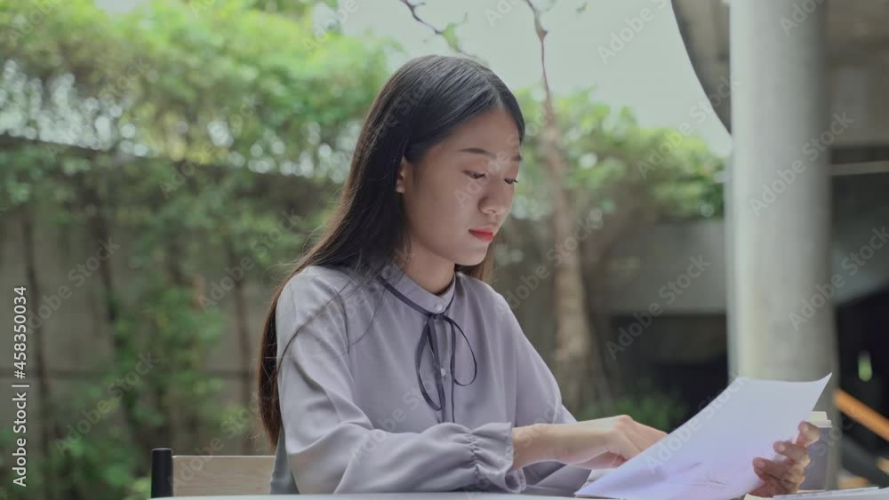 Asian businesswoman sitting outdoors working with laptop and documents.
Asian businesswoman sitting outdoors working with laptop and documents.