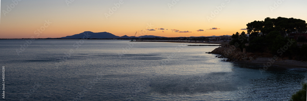 Panoramic view of a sunset of the calm sea with the coastline.