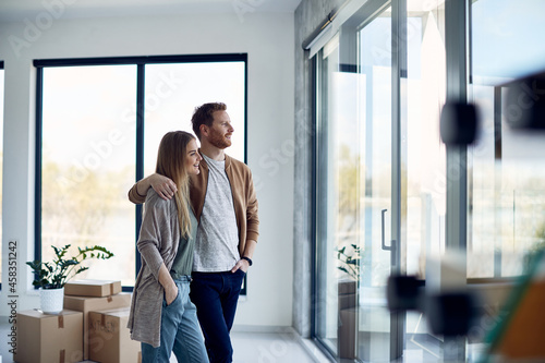 Young happy couple enjoys the view through window at their new home.