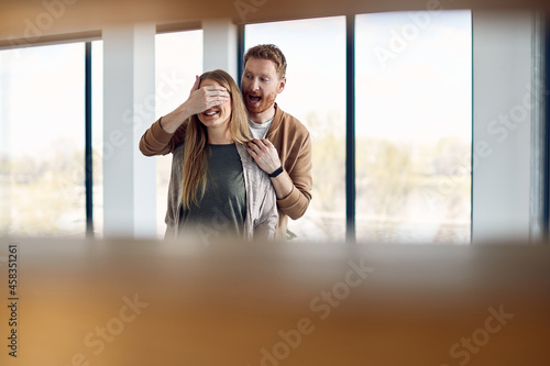 Young excited man covers wife's eyes while surprising her with their new home. photo