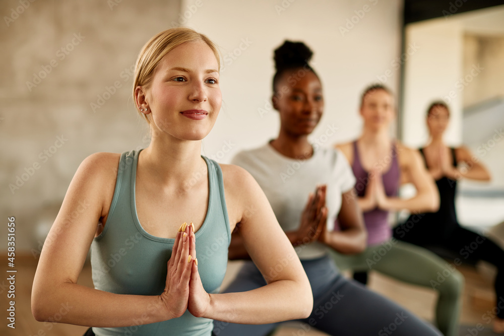 Smiling athletic woman practices Yoga with hands clasped during exercise class at health club.