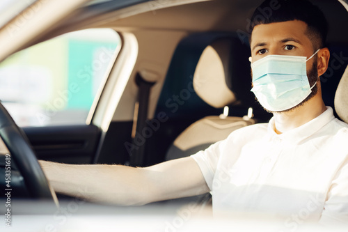 man in a protective medical mask driving a car, the concept of preventing the spread of an epidemic