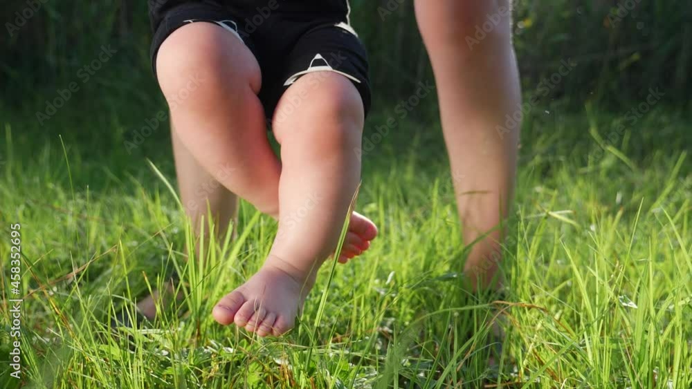 baby does first steps grass happy family. mom helps baby son take steps with his feet. people in the park dream kid concept happy family childhood. child lifestyle son walks barefoot on green grass baby does first steps grass happy family. mom helps baby son take steps with his feet. people in the park dream kid concept happy family childhood. child lifestyle son walks barefoot on green grass