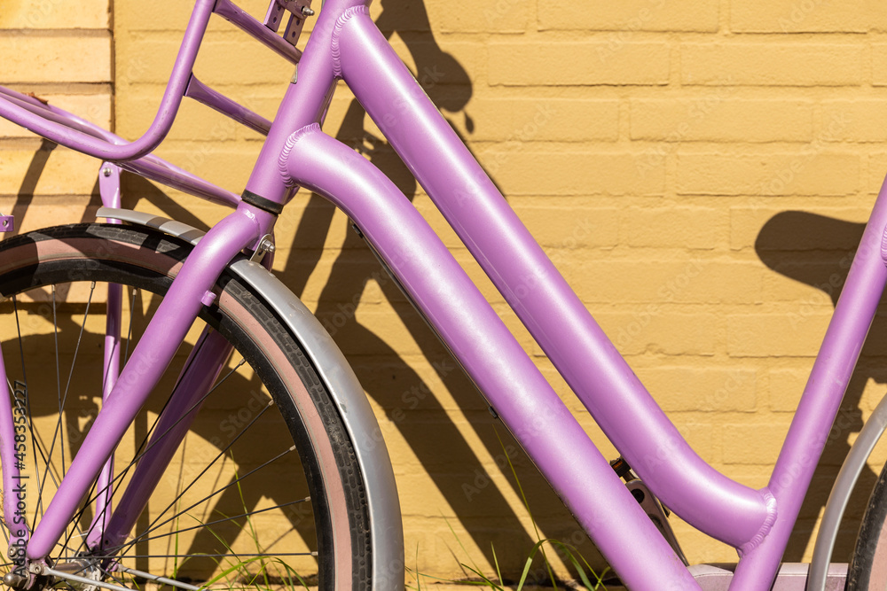 Detail of a colorful lavender purple bike parked in front of a soft yellow colored wall creating a bold happy Dutch scenery on a sunny day during summer in The Netherlands Detail of a colorful lavender purple bike parked in front of a soft yellow colored wall creating a bold happy Dutch scenery on a sunny day during summer in The Netherlands