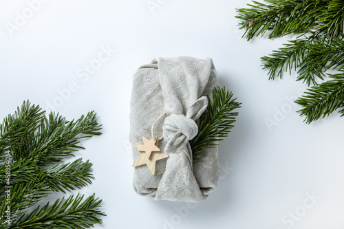 Zero waste Merry Christmas winter gift wrapping in traditional Japanese furoshiki style in linen fabric, decorated with natural green branches of fir nobilis. Concept eco-friendly creative package