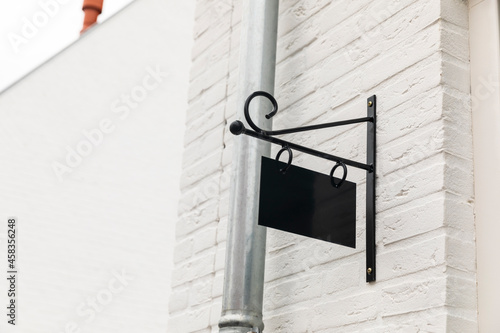 Empty black name sign board hanging on the outside of a white house on the wall near a corner photo