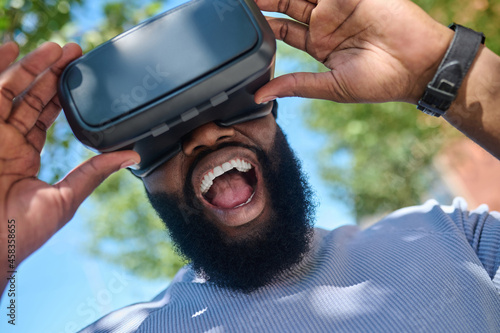 A dark-skinned man in a white tshirt in vr glasses looking excited