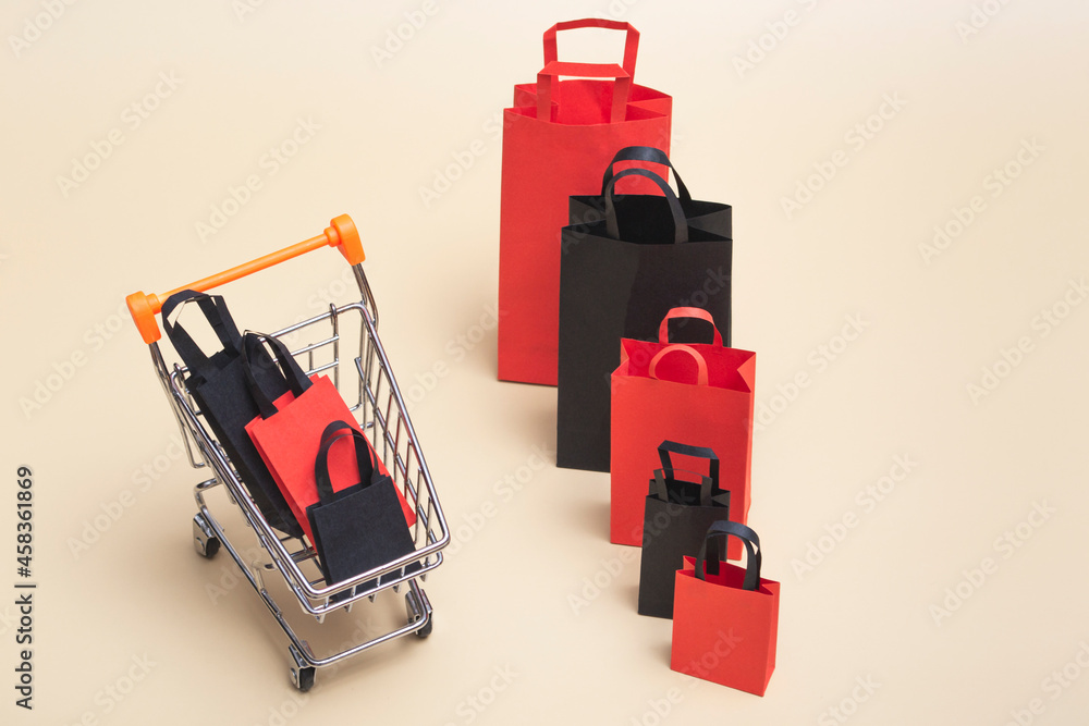 Obraz premium Black friday concept, mockup of paper black and red shopping bags with trolley on colored background. Black Friday sale.