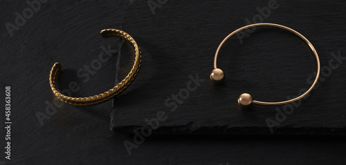 Top view of Two modern gold braid shape bracelets on black stone trays