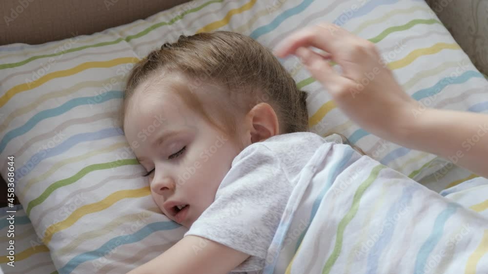 A cute baby sleeps in crib, in nursery in her bed, mother gently covers