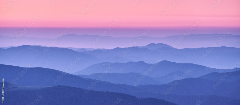 Mountain ridges in fog and pink sky at sunset in autumn. Beautiful landscape with foggy mountain valley, hills, forest at dusk in blue hour in fall. Aerial view of hills. Top view. Nature background - obrazy, fototapety, plakaty 