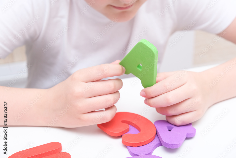 A kid learning letters and alphabet, he is sitting at a table and holding colorful foam letters in hands A kid learning letters and alphabet, he is sitting at a table and holding colorful foam letters in hands