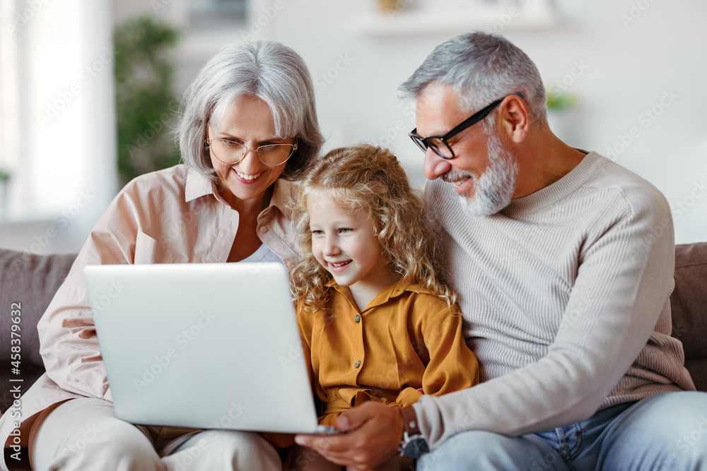 Smiling senior grandparents and cute little girl granddaughter watching cartoons on laptop Smiling senior grandparents and cute little girl granddaughter watching cartoons on laptop