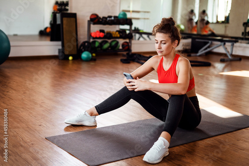 Uses the phone fitness app. A sporty woman and a healthy lifestyle. Comfortable tight-fitting clothing for training. Slim figure cardio classes. An aerobics coach does exercises.
