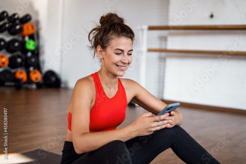 Fototapeta Naklejka Na Ścianę i Meble -  Uses the phone fitness app. Comfortable tight-fitting clothing for training. Slim figure cardio classes. An aerobics coach does exercises. A sporty woman and a healthy lifestyle.