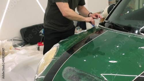 Installation of polymeric protection for paint lacquer of vehicle body tool holds hand man puts vinyl tape on car process of stretching the material. 