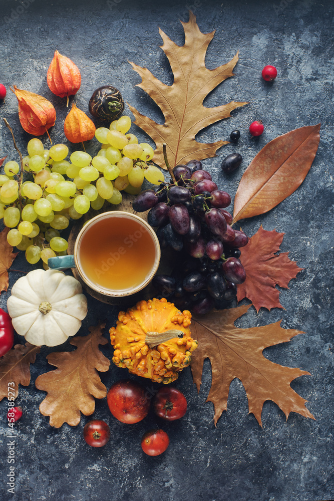 Cozy autumn composition, cup of tea,  pumpkins, grapes, autumn leaves on dark stone table