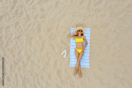 Woman sunbathing on beach towel at sandy coast, aerial view. Space for text photo