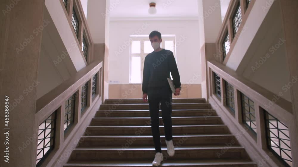 The guy in the mask goes down the stairs in the building. Move one level down. He holds a laptop in his hands. The guy in the mask goes down the stairs in the building. Move one level down. He holds a laptop in his hands.