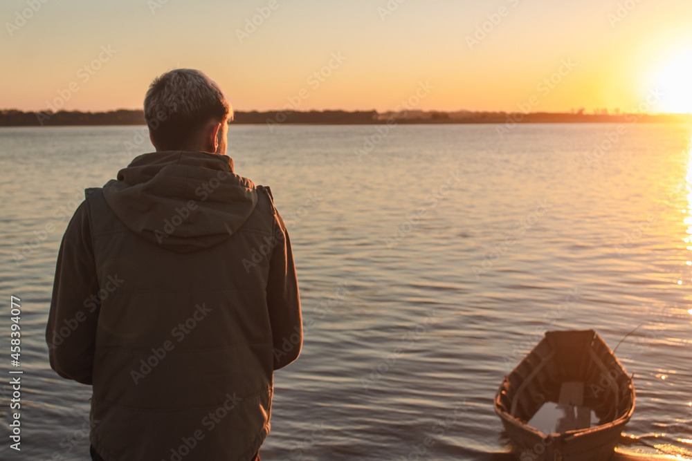Fototapeta premium Young boy appreciating the sunset on the sea shore.