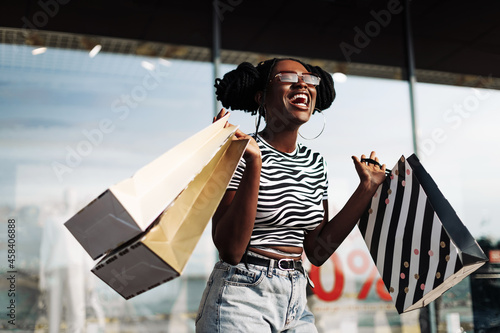 African American woman, wearing sunglasses, standing in a mall with shopping bags in her hands photo