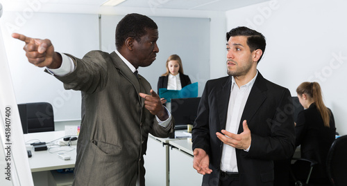 Angry boss pointing his hand at exit in modern office, dismissing frustrated male subordinate