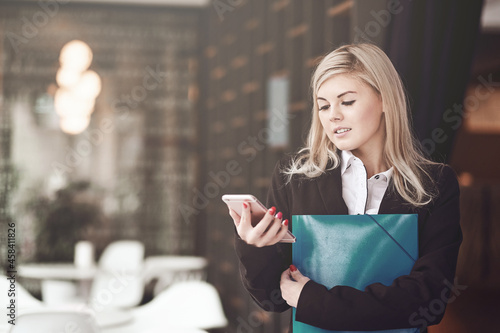 Young business woman writing a message on smart phone and smiling in office