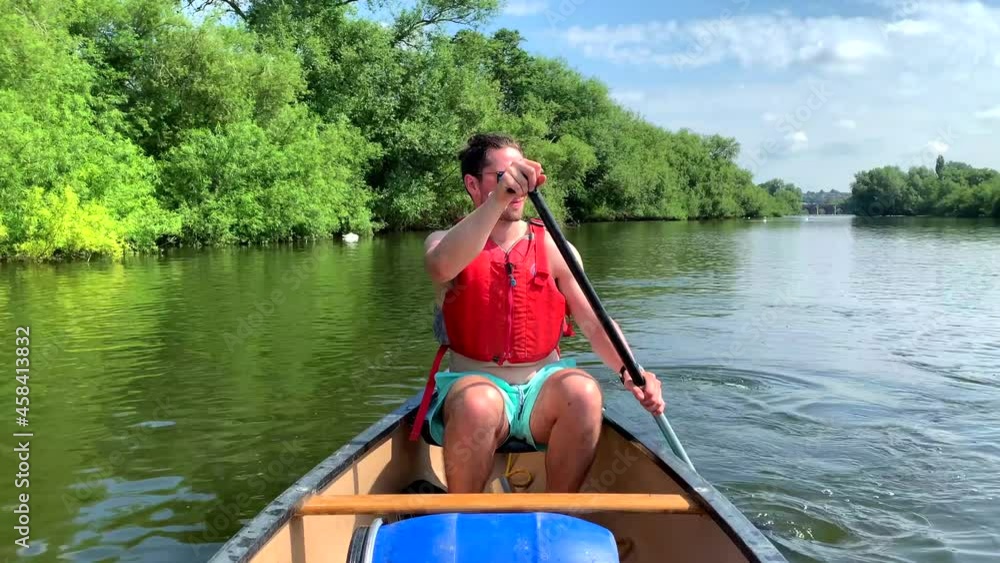 Athletic man in red buoyancy vest paddles canoe on river wye in sun Athletic man in red buoyancy vest paddles canoe on river wye in sun