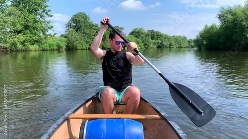 Muscular man paddling canoe on river wye in black top on sunny day photo