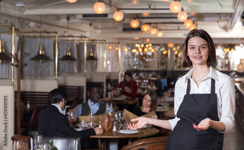 Smiling young waitress warmly welcoming to cozy modern restaurant