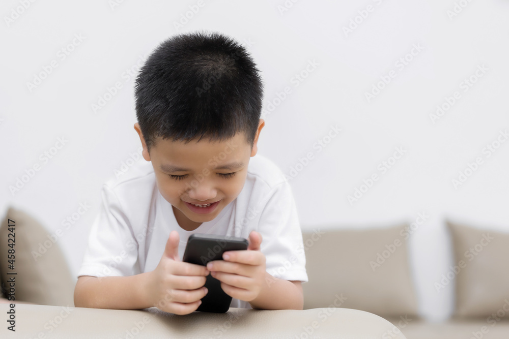 Happy little boy having fun playing game on mobile phone, Preschool kid sitting on sofa with smiling face watching cartoon on smartphone, Child using cell phone while relaxing at home Happy little boy having fun playing game on mobile phone, Preschool kid sitting on sofa with smiling face watching cartoon on smartphone, Child using cell phone while relaxing at home