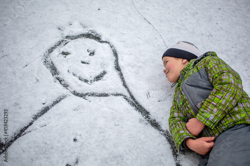 happy boy lies in the snow near the drawn picture