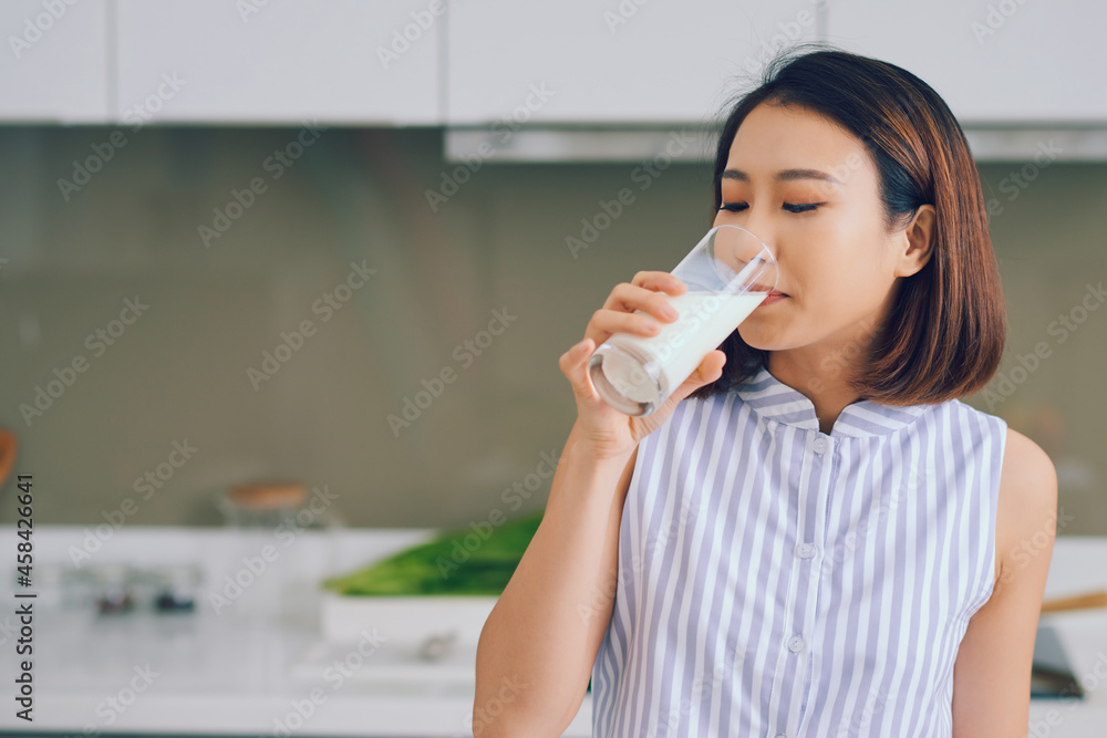 Portrait of young Asian woman drinking milk while standing in the kitchen. Portrait of young Asian woman drinking milk while standing in the kitchen.